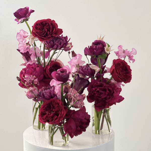 Three small glass vases hold magenta and pink flowers.
