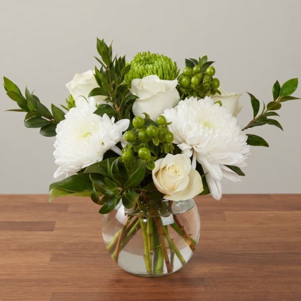 White roses and chrysanthemums in a clear glass vase with green berries