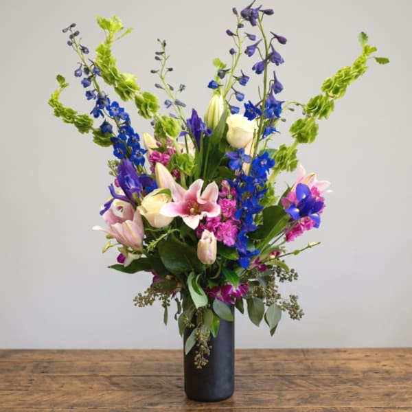Tall mixed bouquet in a black vase with pink lilies and blue flowers