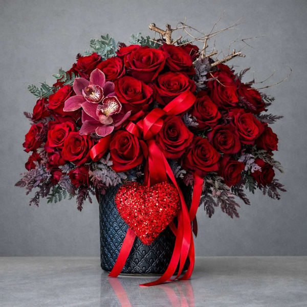 Red rose arrangement in a dark vase with a ribbon and heart decoration