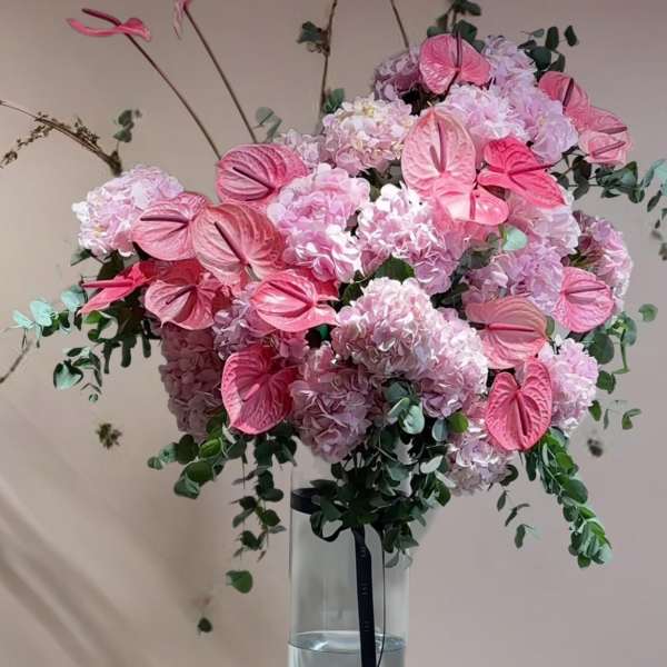 Pink hydrangea arrangement with anthuriums in a tall glass vase