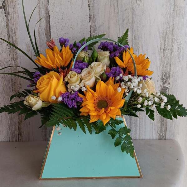Bouquet of orange sunflowers, cream roses, and purple filler in a turquoise box