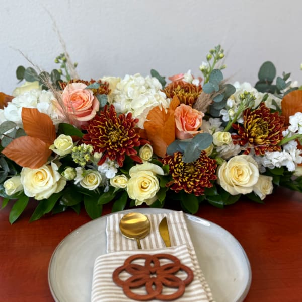 Low floral centerpiece with cream roses, peach roses, and burgundy mums on a table