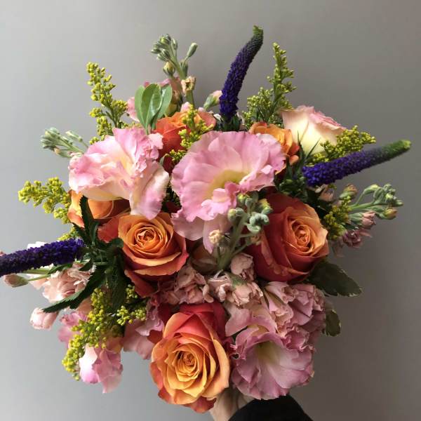 Handheld bouquet of pink and orange roses with purple spikes