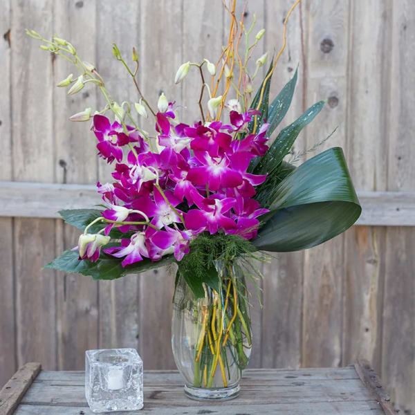 Purple orchid arrangement in a clear glass vase with broad leaves