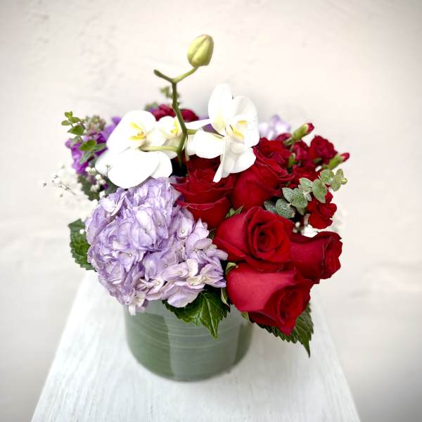 Red roses, lavender hydrangea, and white orchids in a green vase