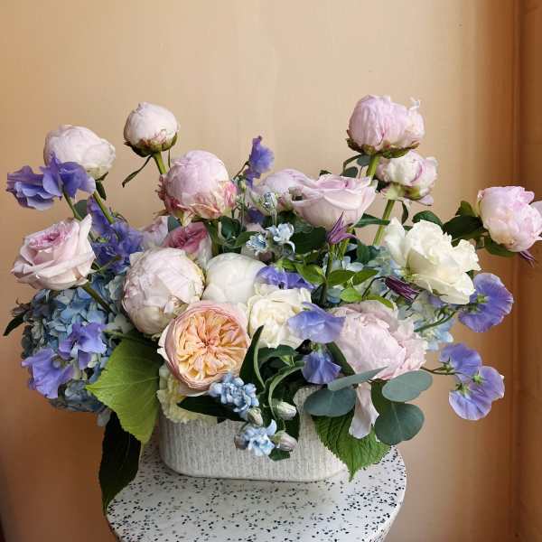 Pastel bouquet of roses, peonies, and blue flowers in a white vase