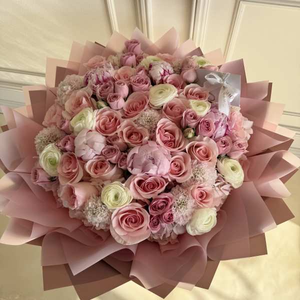 Large pink bouquet of roses and ranunculus wrapped in pink paper