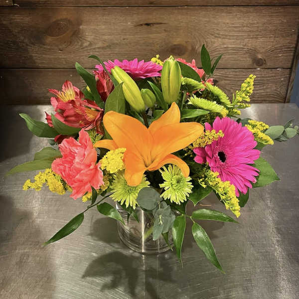 Mixed bouquet with orange lily, pink gerberas, and yellow filler in a glass vase