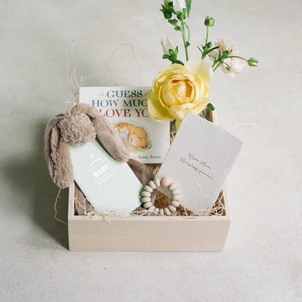 Gift box with a yellow flower, baby book, plush bunny ears, and a card