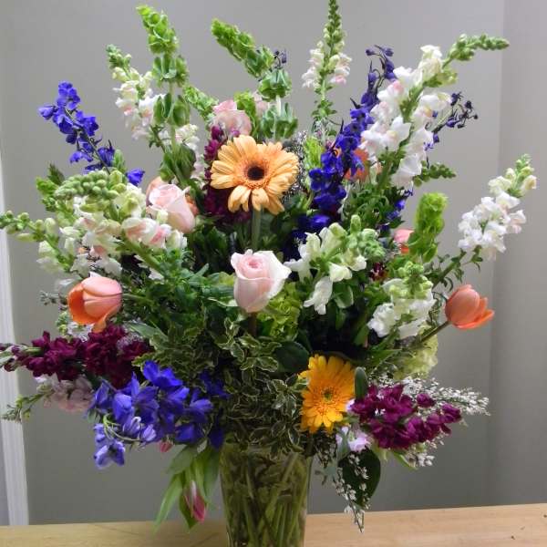 Tall mixed bouquet in a clear glass vase with pink, white, purple, and orange blooms