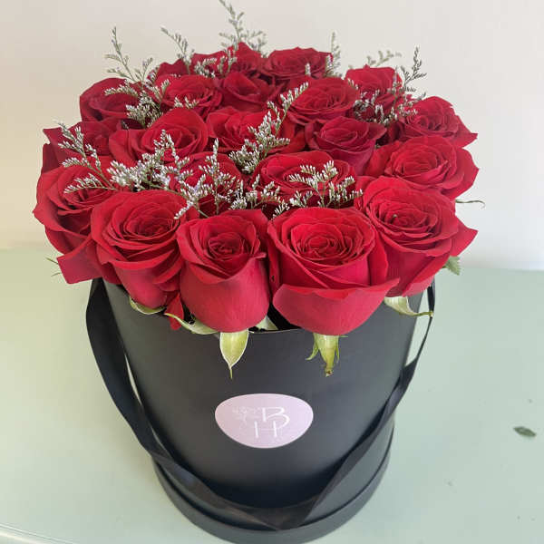 Red roses arranged in a black hatbox with silver filler sprigs