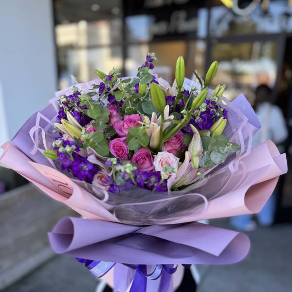Bouquet of pink roses and purple flowers wrapped in lavender paper