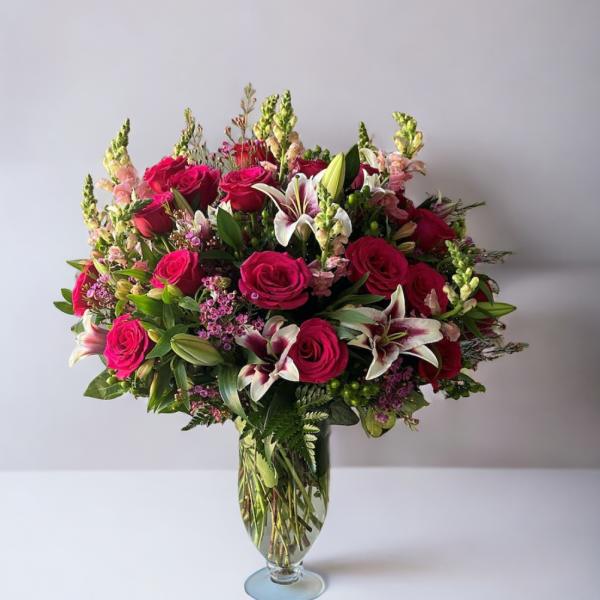 Tall arrangement of hot pink roses and white lilies in a clear glass vase