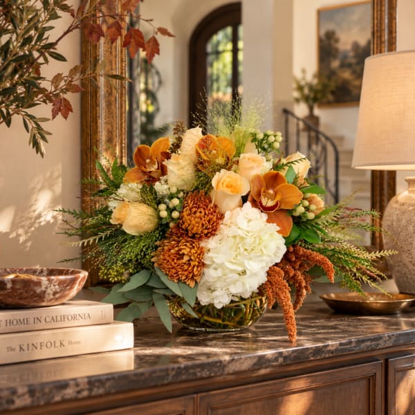 Autumn floral arrangement in a glass bowl with orange, cream, and white blooms