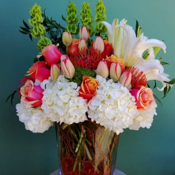 Mixed bouquet of roses, lilies, hydrangeas, and tropical blooms in a glass vase