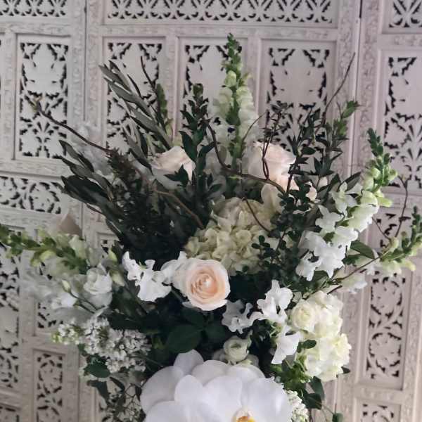 White floral arrangement with orchids and roses in a green vase