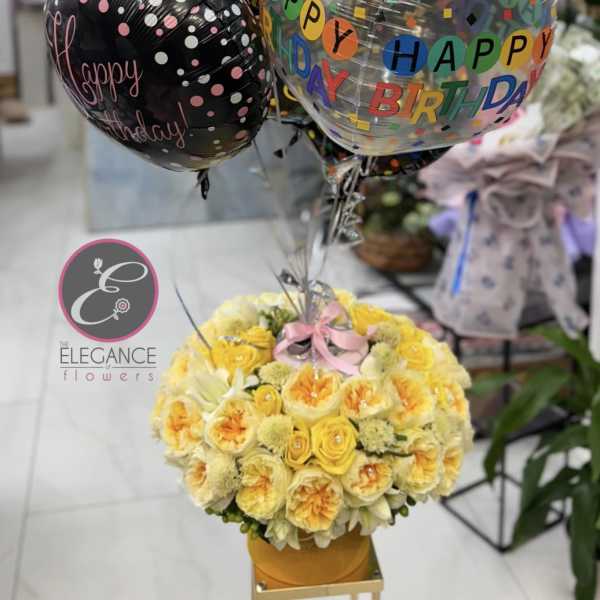 Birthday balloon bouquet above a yellow floral arrangement