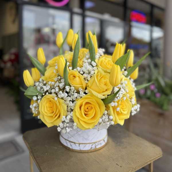 Yellow roses and tulips arranged in a round white box