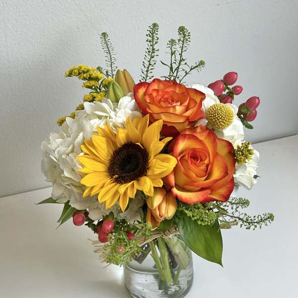 Bouquet of orange roses, a sunflower, and white hydrangeas in a glass vase