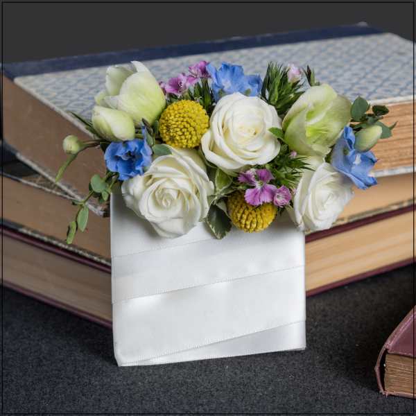 White roses and blue flowers arranged in a white ribbon-wrapped holder