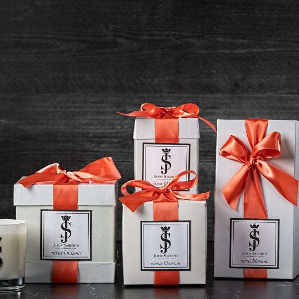 Gift boxes with orange ribbons beside a candle and white flowers in a vase