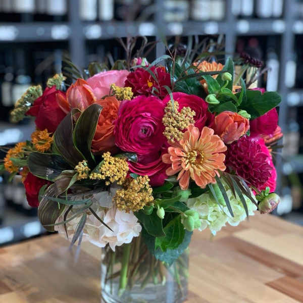 Mixed bouquet of pink, orange, red, and white flowers in a clear glass vase