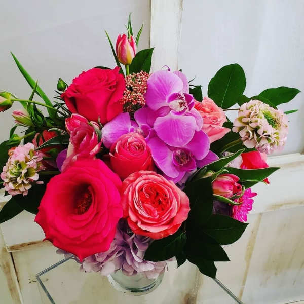 Bouquet of pink roses, orchids, and tulips in a glass vase