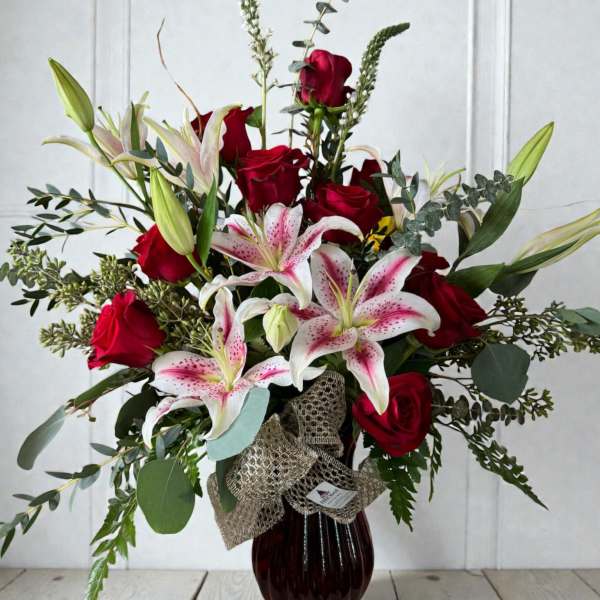 Red roses and pink stargazer lilies in a dark glass vase