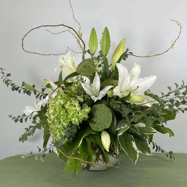 White lilies and green hydrangea in a glass vase with curly branches