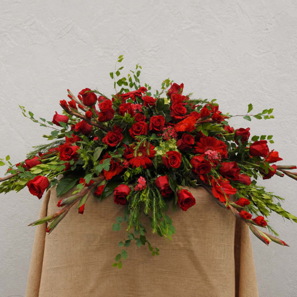 Large red rose arrangement with mixed greenery on a draped stand