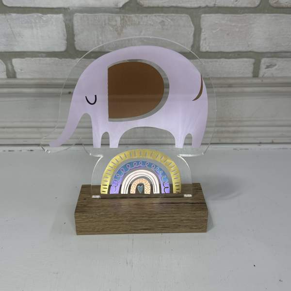 A clear acrylic elephant-shaped decor piece on a wood base with a small rainbow design