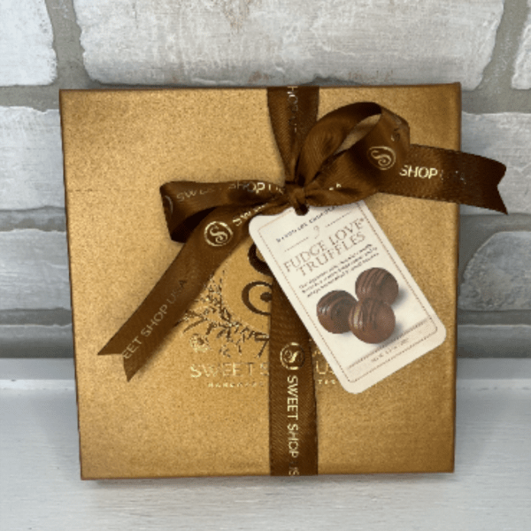 Gold chocolate gift box tied with brown ribbon and a truffle tag on a light background