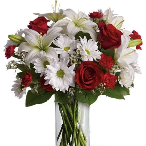 Red roses and white lilies with daisies in a clear glass vase