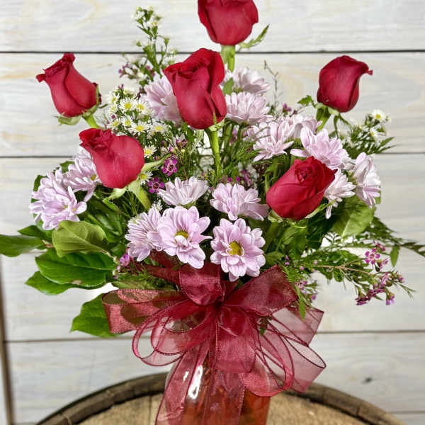 Red roses and pale pink daisies in an amber vase with a red ribbon