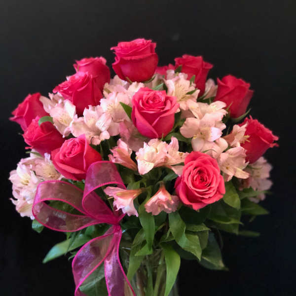 Pink roses and pale alstroemeria in a glass vase with a pink ribbon