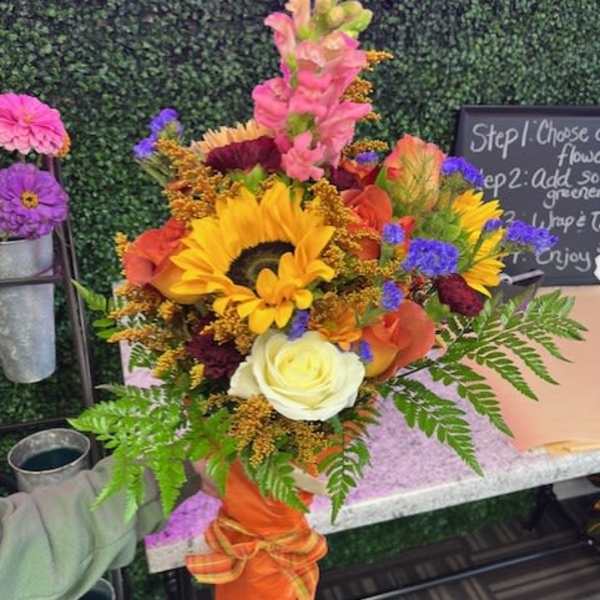 Bright mixed bouquet with sunflowers, roses, and snapdragons in an orange wrap
