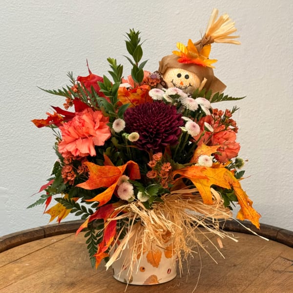 Fall floral arrangement with a scarecrow topper in a decorated vase