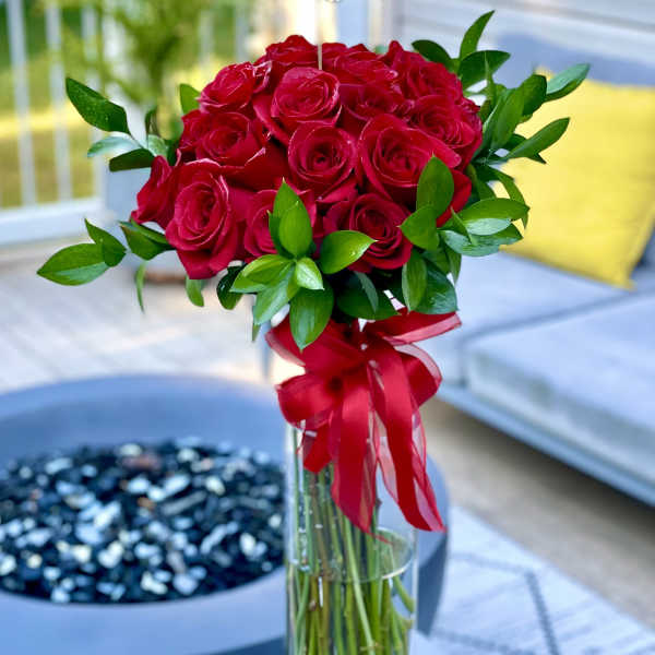 Red rose bouquet in a tall glass vase with a red ribbon