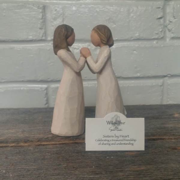 Two small figurines of girls facing each other and holding hands
