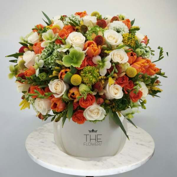 Mixed bouquet of orange, white, and green flowers in a white vase