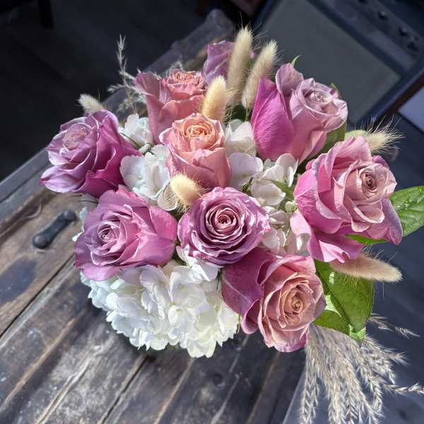 Pink and lavender roses with white hydrangeas in a compact bouquet