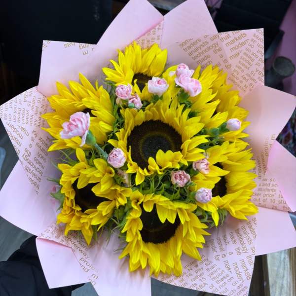 Bouquet of yellow sunflowers with small pink spray roses in pink paper