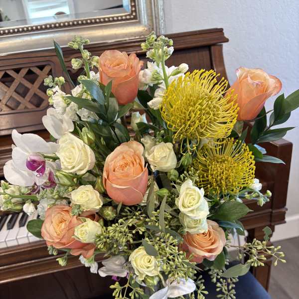 Mixed bouquet of peach roses, white orchids, and yellow pincushion blooms in a glass vase