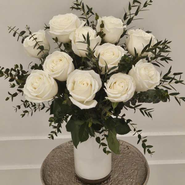 White roses arranged in a white vase with dark greenery