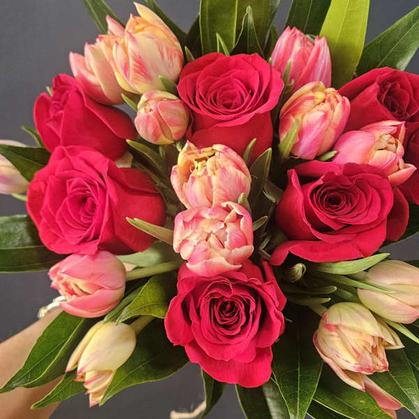 Hand-tied bouquet of hot pink roses and cream-pink tulips against a dark background