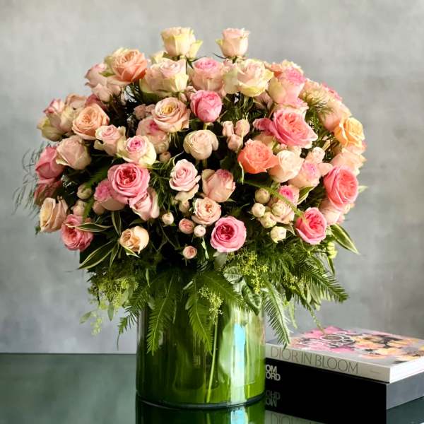Large arrangement of pink and peach roses in a green glass cylinder vase on a table