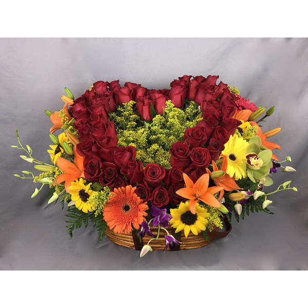 Heart-shaped red rose arrangement in a basket with orange and yellow flowers