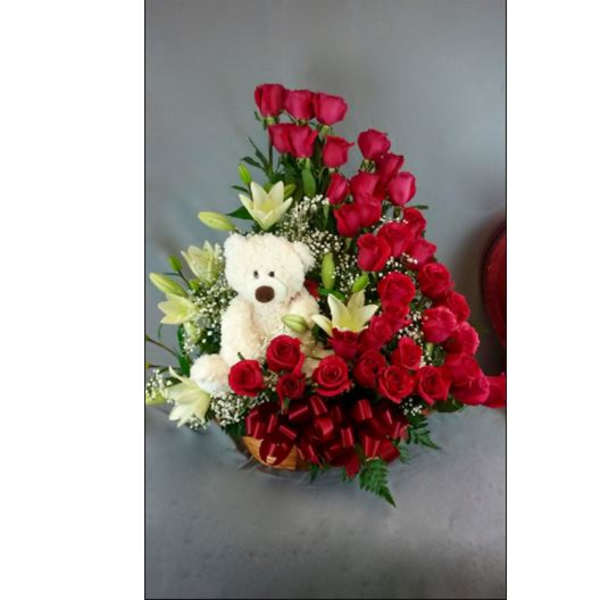 Red roses and white lilies arranged with a teddy bear in a basket