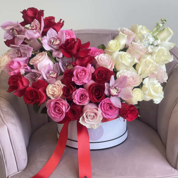 Large bouquet of red, pink, and white roses with orchids in a round box